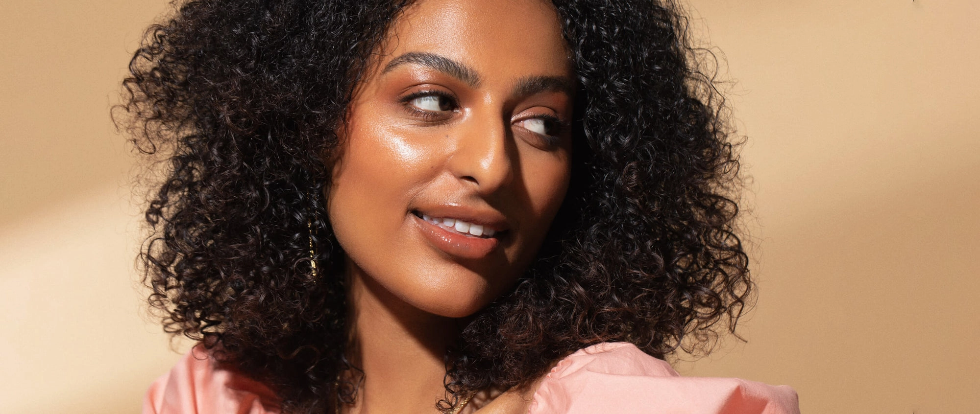 Portrait of a woman with curly hair looking over her shoulder, glowing skin